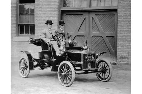 Dwóch dżentelmenów w melonikach siedzi w zabytkowym Fordzie Model T Runabout, gotowych na przejażdżkę.