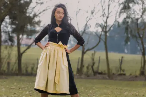 Junge Frau im Dirndl mit einer hellgelben Dirndlschürze aus Leinen, die im Freien steht.