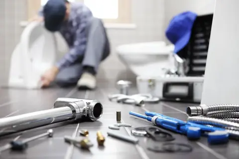 Idraulico al lavoro su un water, con attrezzi e tubi in primo piano. La pendenza scarico cucina è fondamentale per un corretto deflusso.