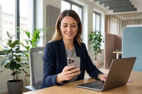 Donna sorridente al telefono, con un laptop aperto. Sembra che stia organizzando la sua astensione dal lavoro.