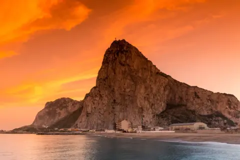 Gibraltar, czy to państwo, majestatycznie wznosi się nad morzem o zachodzie słońca. Pomarańczowe niebo maluje dramatyczne tło dla skalistej skały.