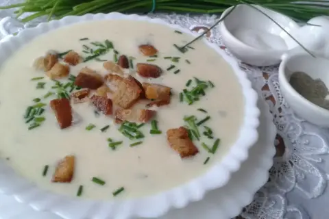Kremowa zupa porowa z grzankami i szczypiorkiem w białej misce.