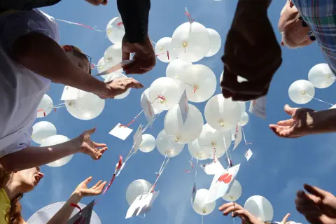 Gäste lassen bei einer Hochzeit weiße Luftballons mit Wünschen in den Himmel steigen.