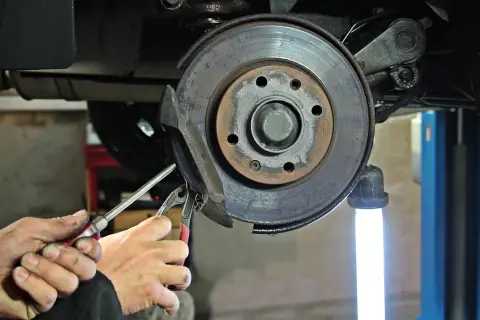 Mains d'un mécanicien utilisant des outils pour changer un disque de frein usé sur une voiture.