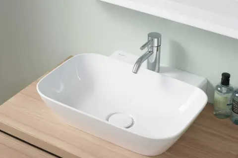 Nowoczesna, mała umywalka do WC na drewnianym blacie, z chromowaną baterią i dwoma buteleczkami płynu do rąk.