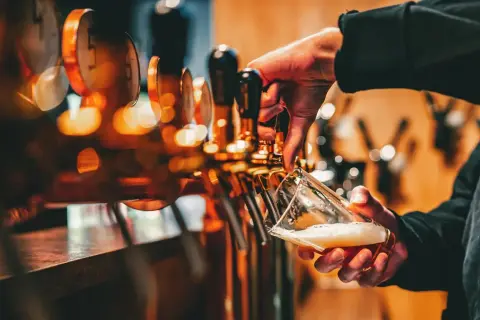 Mano che versa birra da una spillatrice, creando una schiuma perfetta. La spillatura alla tedesca è un'arte.