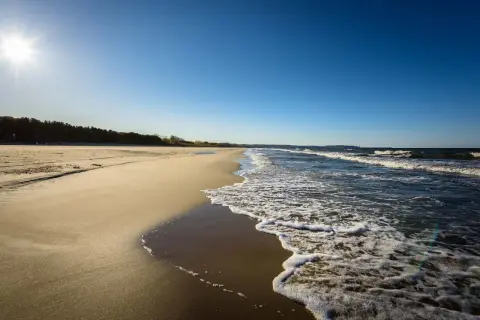 Słoneczny dzień nad polskim morzem. Piaszczysta plaża, szum fal i błękitne niebo tworzą idealny krajobraz.