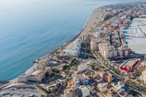 Vista aérea de la costa de Almería, Roquetas de Mar, con el mar azul, la playa, edificios residenciales y un castillo histórico.