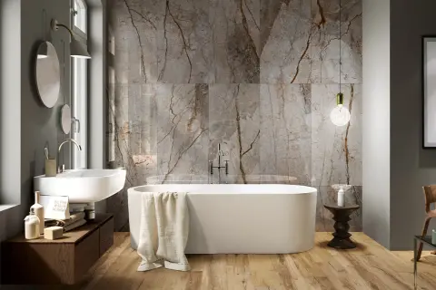 Bagno moderno con vasca freestanding, lavabo sospeso e parete in marmo con venature che si abbinano al legno del pavimento. Idee bagno marmo e legno per un ambiente di lusso.