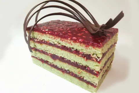 Gâteau pistache framboise mascarpone, une tranche aux couches vertes et rouges, garnie de chocolat.
