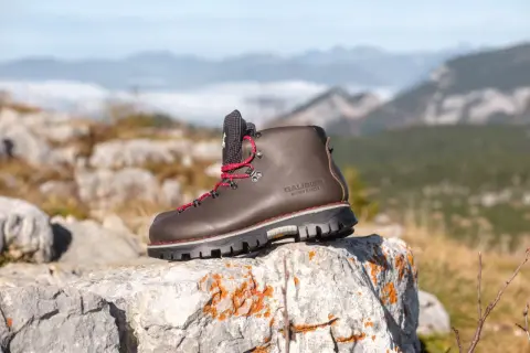 Une bonne chaussure de marche marron, lacets rouges, sur un rocher, avec des montagnes brumeuses en arrière-plan.
