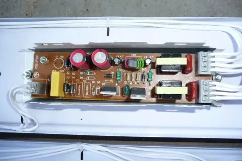 Elektroniczny statecznik z kondensatorami, transformatorami i innymi elementami na płytce drukowanej, podłączony białymi przewodami.