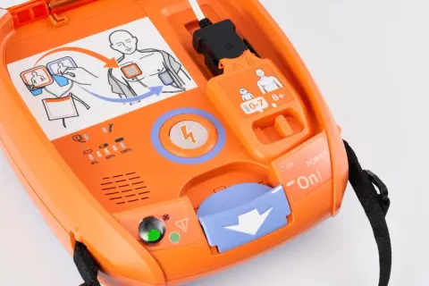 Pomarańczowy AED gotowy do użycia. Schemat pokazuje, jak prawidłowo umieścić elektrody do defibrylacji.