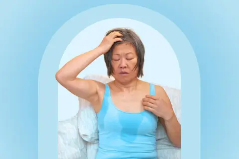 A woman experiencing night sweats after working out, with sweat visible on her tank top and forehead.