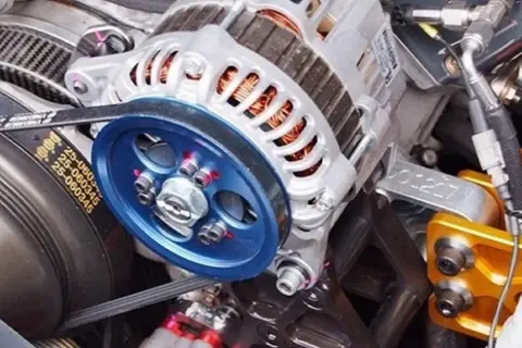 Detalle de un alternador de coche, listo para cambiar. Se aprecian la polea azul y la correa.