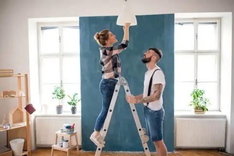 Coppia installa un lampadario, una delle migliorie che aumentano il valore di un immobile.
