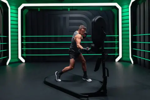 A man in boxing gloves practices his jab and cross, demonstrating proper boxing terminology in a futuristic ring with neon green accents.