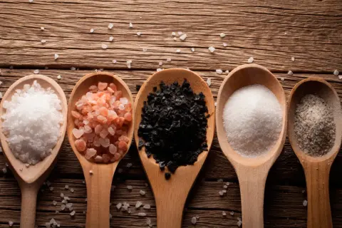 Cinco cucharas de madera muestran una composición de la sal: blanca gruesa, rosa del Himalaya, negra, fina blanca y con hierbas.