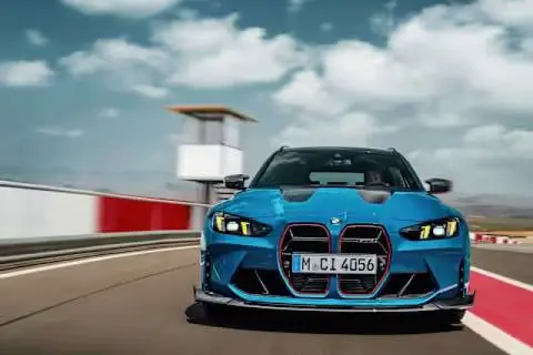 Niebieskie BMW M3 Touring pędzi po torze wyścigowym, chmury na niebie dodają dynamiki.
