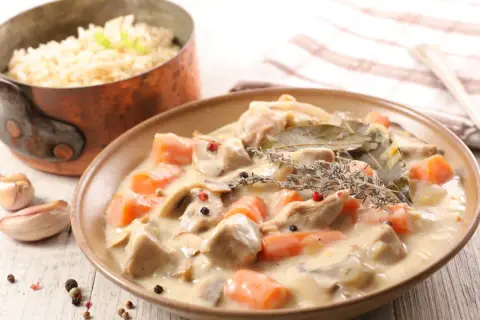 Un delicioso blanquette de ternera con zanahorias y champiñones en una cremosa salsa, servido con arroz blanco.