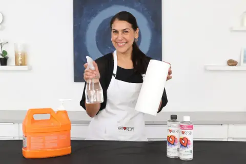 Mujer sonriente muestra cómo limpiar la resina epoxi de los utensilios con spray y papel.