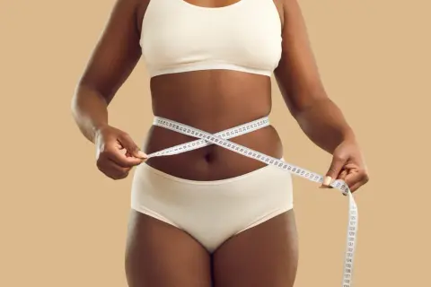 Une femme mesure sa taille avec un mètre ruban, symbolisant son objectif de perdre 5 kilos en 1 mois.