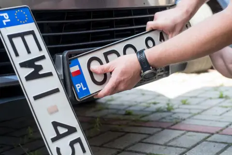 Ręce montują polską tablicę rejestracyjną. Nowe oznaczenie pojazdu gotowe do drogi.