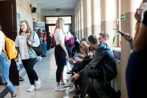 Uczniowie w szkolnym korytarzu, niektórzy siedzą, inni idą. Czy to sigma?