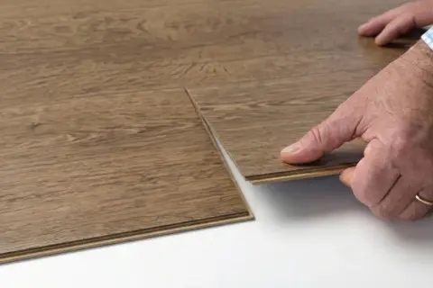 Close-up of a hand performing vinyl floor installation, clicking two wood-look planks together.