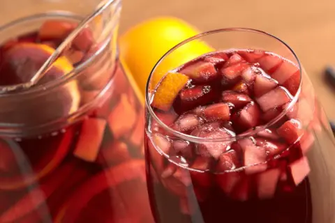 Un bicchiere e una caraffa pieni di vino per sangria, con pezzi di frutta e fette d'arancia.