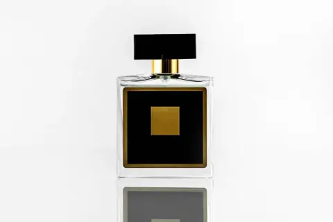 Elegancka szklana butelka perfum z czarną etykietą i złotym kwadratem.