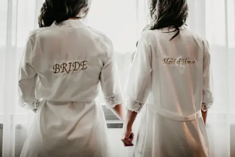 Dwie kobiety w szatach, jedna z napisem "BRIDE", druga "Maid of Honor". Idealny obrazek, by zainspirować się, jak poprosić świadka na ślub.