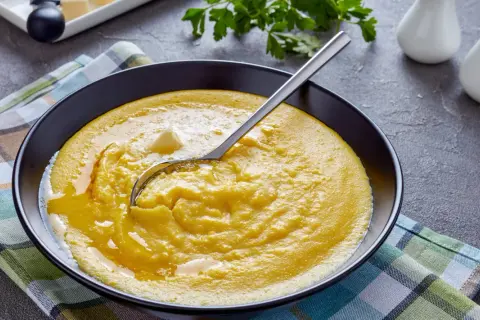 Cremige Polenta mit Butter in einer schwarzen Schüssel, bereit für ein köstliches polenta rezept. Ein Löffel ruht darin.