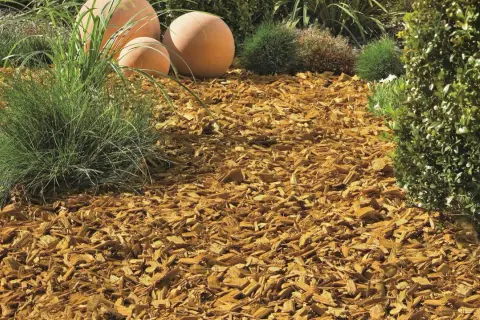 Ein schön angelegtes Beet mit Rindenmulch, Ziergräsern und dekorativen Kugeln.