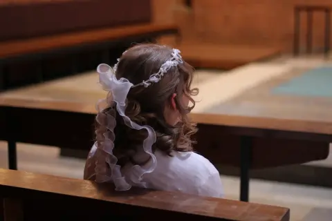 Dziewczynka w białej sukience i wianku na głowie siedzi w kościele. Czy nie przyjęcie komunii jest grzechem?