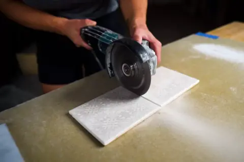 Hands carefully cutting decorative porcelain tile with an angle grinder, creating a clean line.