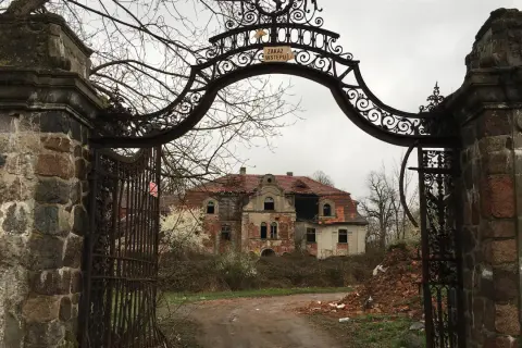 Zrujnowany pałac w glince, zniszczona brama i dziki ogród.