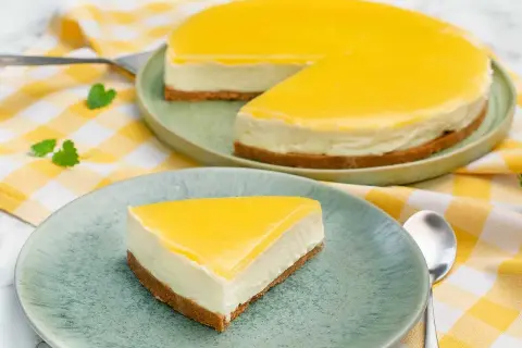 En krämig cheesecake med en syrlig lemon curd-topping. En bit serverad på en tallrik bredvid en hel cheesecake.