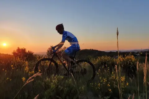 Ciclista in azione al tramonto sul Monte Grimano, tra erba alta e fiori gialli.
