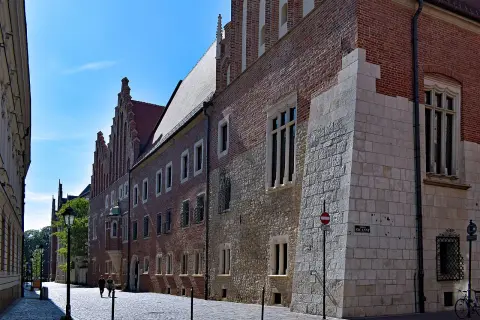 Kamienne i ceglane mury Collegium Maius w Krakowie, z charakterystycznymi oknami i detalami architektonicznymi, na tle błękitnego nieba.