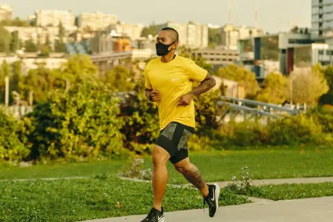 Man running with oxygen mask on a path, city skyline in background.