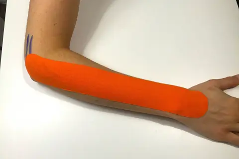 Pomarańczowy plaster kinezjotaping na przedramieniu, wspierający ćwiczenia na łokieć tenisisty.