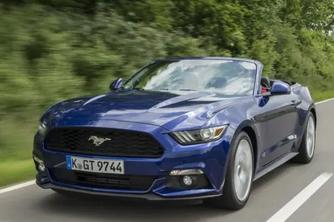Błękitny mustang cabrio pędzi po krętej drodze wśród zieleni.