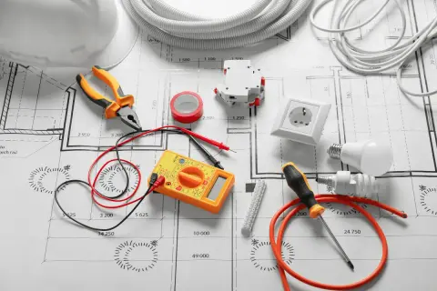 Outils d'électricien et composants sur un plan, pour un devis électricité exemple. Pince, multimètre, prise, ampoules, disjoncteur, ruban adhésif.
