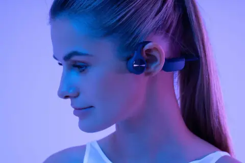 Profil d'une femme portant un casque à conduction osseuse bleu, éclairée par des lumières bleues et roses.