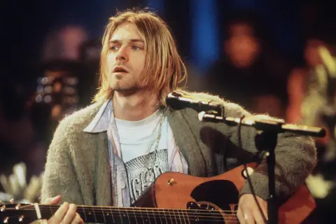 Kurt Cobain spielt Akustikgitarre, ein ikonisches Bild, das an eine verstorbene Rockmusiker Liste erinnert.