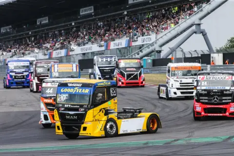 Des camions de course colorés s'affrontent lors d'un grand prix camion, sous les yeux d'une foule en délire dans les tribunes.