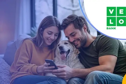 Szczęśliwa para z psem przegląda ofertę velo bank kredyt hipoteczny na telefonie.