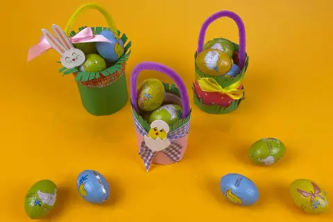 Tre cestini di Pasqua fai da te, decorati con coniglietti e pulcini, pieni di uova di cioccolato.