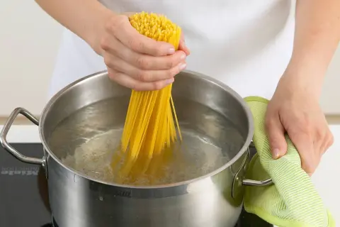 Hände halten Spaghetti, um sie in kochendes Wasser zu geben. Nudeln kochen ohne Herd ist hier nicht zu sehen, aber das Wasser brodelt.